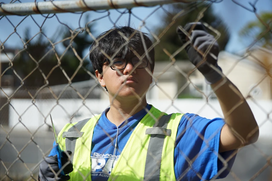 Boy in a yellow reflective vest behind a chainlink fence